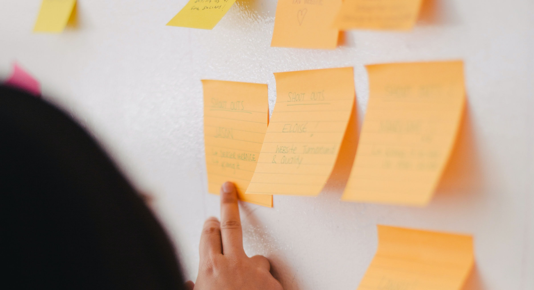 Post-it notes on a white board with a finger pointing to one, and person's hair in the foreground